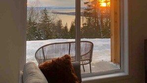 Una habitación con un amplio ventanal que da a un paisaje nevado y una puesta de sol.