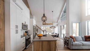 Una cocina moderna con armarios blancos, una isla de madera y un comedor con un sofá gris y un plaid estampado.