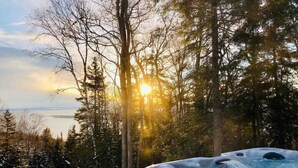 Un jacuzzi en un bosque nevado con vistas a la puesta de sol sobre un cuerpo de agua.