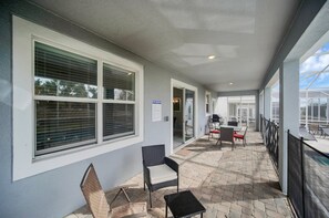 Een overdekt buitengebied met een patio tafel, stoelen, een barbecue en een bordje dat een patio/zwembadzone aangeeft.