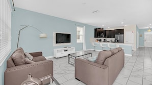 Uma sala de estar moderna com sofá, televisão e cozinha equipada com frigorífico e micro-ondas.