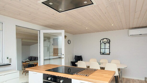 A compact kitchen with a built-in stove, a dining area with a white table and chairs, and a visible clock on the wall. - 4 Star Holiday Home in Aabenraa (Aabenraa)