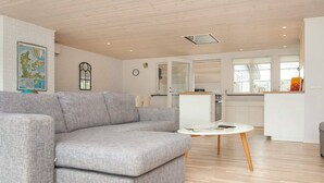 A modern living room with a grey sectional sofa, a small white round table, and a kitchen area in the background. - 4 Star Holiday Home in Aabenraa (Aabenraa)