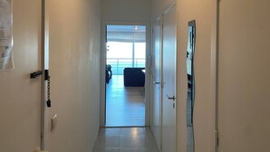 Un pasillo estrecho con paredes y puertas blancas, que conduce a un balcón con vistas al mar.