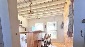 A kitchen with wooden flooring, a bar area with stools, and a window providing natural light. - Lillian’s blackberry cabin (Ava)