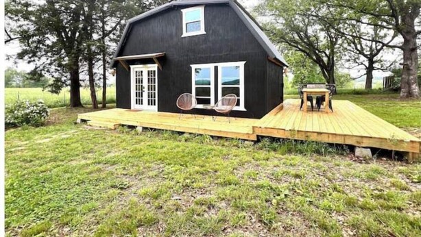 A black house with a wooden deck, two doors, and two windows. - Lillian’s blackberry cabin (Ava)