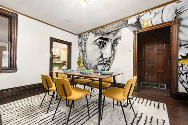 Comedor con un mural, sillas amarillas, una mesa de madera y un tapete estampado.