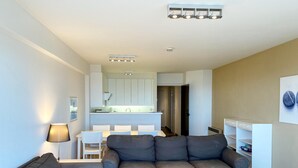 A modern living room with a grey sofa set, a white coffee table, and a dining area with white chairs. - Apartment in Nieuwpoort by the Beach (Nieuwpoort)