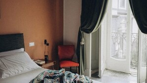 Hotellihuone, jossa on sänky, tuoli, yöpöytä ja ikkuna, jossa on verhot.