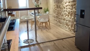Una cocina con suelo de madera, pared de piedra y zona de comedor con sillas blancas y una mesa.