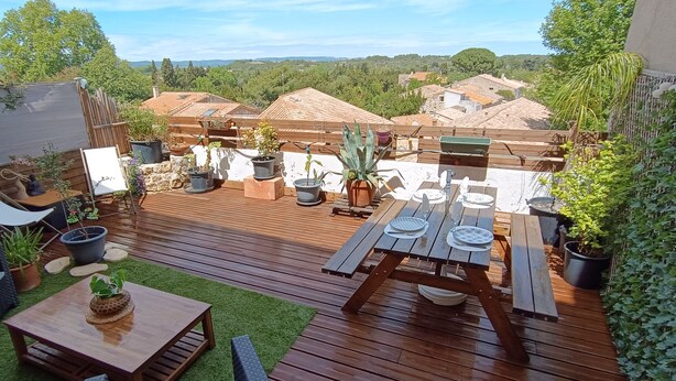 Un patio exterior con piso de madera, una mesa de madera y varias plantas en macetas.