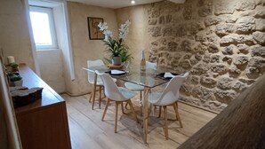 Comedor con mesa de vidrio, sillas blancas, planta en maceta y pared de piedra.