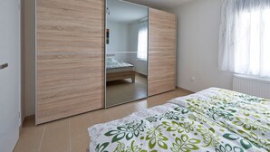 A bedroom with a large wardrobe, a bed with a floral bedspread, and a window with sheer curtains. - Rheinflair Comfortable Holiday Residence (Kamp-Bornhofen)