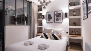 Ein modernes Hotelzimmer mit einem großen Bett, einer Kristallleuchter, Kunstwerken an den Wänden und einer eingebauten Ablage mit Dekoration.