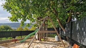 Ein Spielplatz aus Holz mit Schaukel, Rutsche und Sandkasten sowie einer Sitzbank.