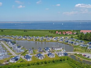 A coastal residential area with modern houses, a lake, and sailboats in the distance. - House in Zeeland Near the Dyke (Wemeldinge)