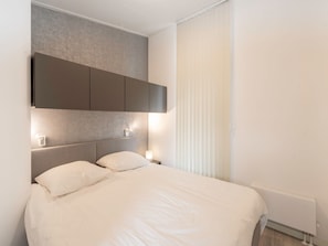 A modern bedroom with a large bed, a headboard with built-in lighting, and a window with blinds. - House in Zeeland Near the Dyke (Wemeldinge)