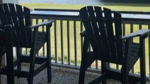 A balcony with two Adirondack chairs facing a lake and forested area.