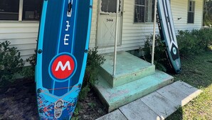 A blue surfboard with a red logo and the number 5444 in front of a house with a porch.