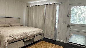 A bedroom with a bed, a bedside table, a window with curtains, and a door.