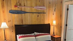 A bedroom with a wooden wall, a bed with striped bedding, two bedside tables with lamps, and a ceiling fan.