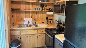 A compact kitchen with wooden cabinetry, a stainless steel sink, a stove, and a black refrigerator.