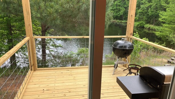 A wooden deck with a view of a lake, a grill, and a grill cover.