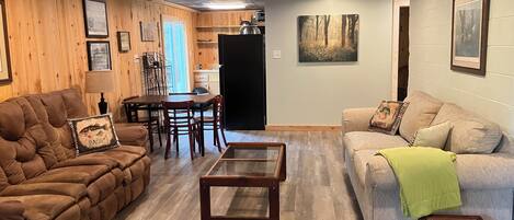 A cozy living room with a brown sofa, a grey couch, a wooden coffee table, and a dining area with a table and chairs.