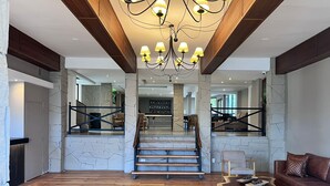 A spacious living area with a wooden floor, a staircase leading to another level, a modern chandelier, and a stone wall. - Cerro Calafate Hotel (El Calafate)