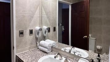 Un baño moderno con encimera de granito, un lavabo blanco, un espejo grande y un perchero.