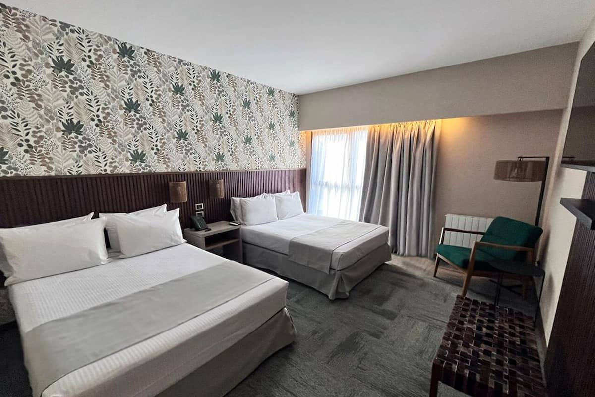 Una habitación de hotel con dos camas, un escritorio, una silla y un papel tapiz estampado.