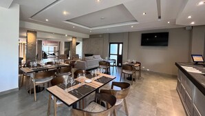 A spacious dining area with multiple tables set for a meal, a kitchen area with a large TV, and a seating area with a sofa and chairs. - Cerro Calafate Hotel (El Calafate)
