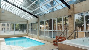 An indoor swimming pool with a glass ceiling, a hot tub, and a wooden bench. - Cerro Calafate Hotel (El Calafate)