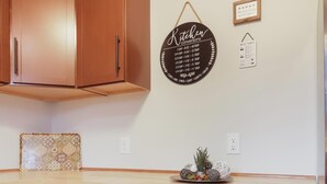 Una cocina con armarios de madera, un letrero circular con indicaciones para la cocina, una pequeña cita enmarcada y un plato decorativo sobre la encimera.