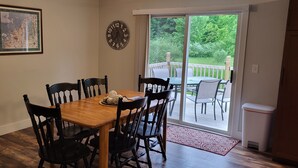 Un comedor con una mesa y sillas de madera, un mapa enmarcado en la pared, un reloj y vistas a una terraza a través de una puerta de cristal.