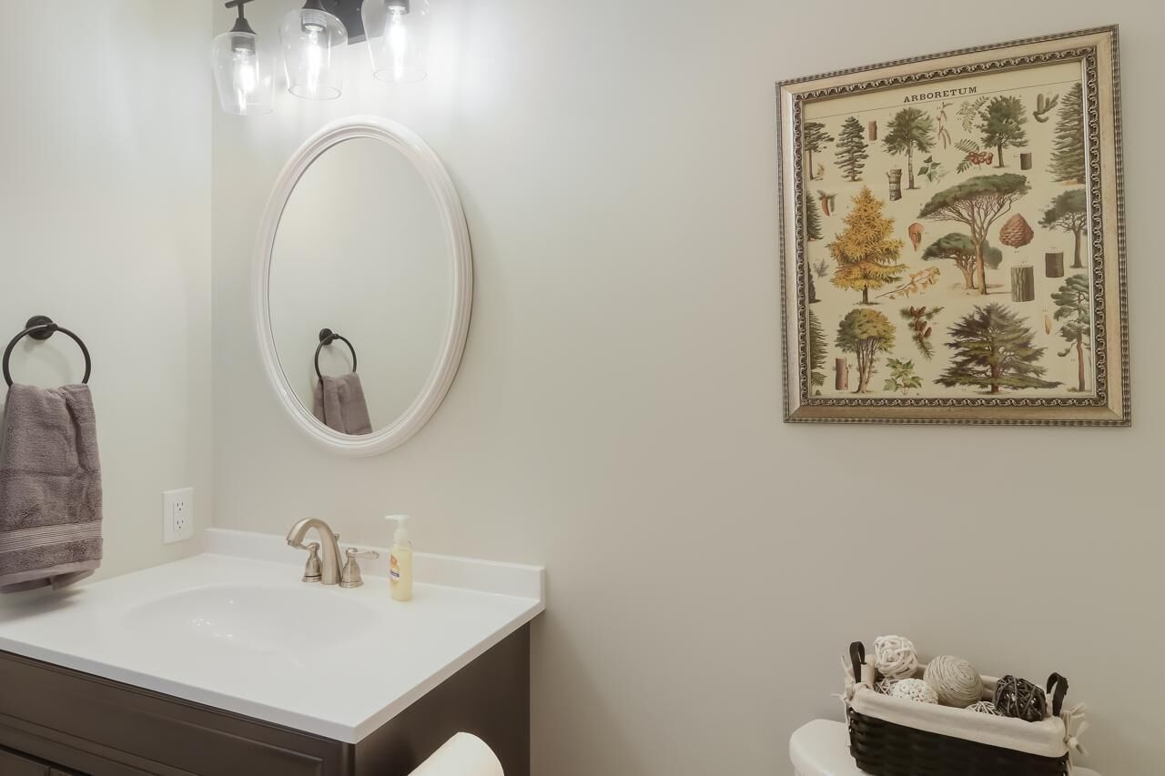 Een badkamer met een witte wasbak, een spiegel en een ingelijste botanische print aan de muur.