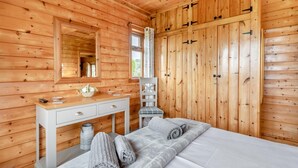 En stuga med träpanel, inredd med en säng, en byrå, en spegel och en garderob.