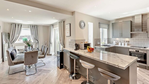 A modern kitchen with a central island, bar stools, and a dining area with a table and chairs.