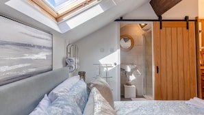 Un dormitorio con tragaluz, una cama con ropa de cama floral, una mesita de noche, un espejo y una puerta de madera.