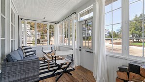 Une véranda avec un canapé en osier, un tapis à rayures et une table en bois.