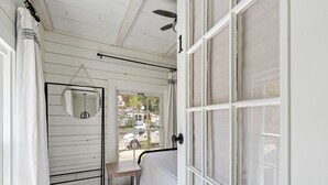 Une chambre à coucher avec un lit, une petite table, un miroir suspendu et une fenêtre donnant sur la rue.
