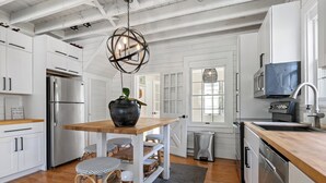 Une cuisine moderne avec des meubles blancs, des appareils en acier inoxydable, une table en bois et des chaises en osier.