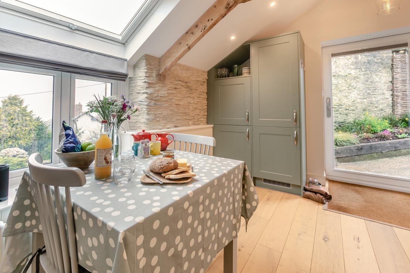 Un coin repas avec une table mise pour le petit-déjeuner, une fenêtre donnant sur un paysage verdoyant et un buffet gris contenant de la verrerie.