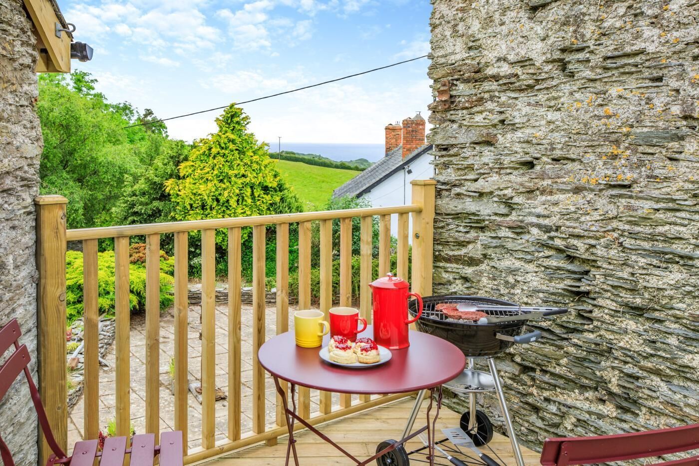 A balcony with a table set for a meal, a grill, and a view of a green landscape.