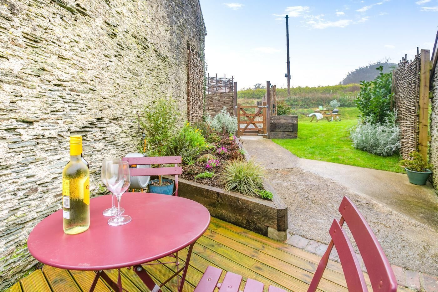 Une terrasse avec une table et des chaises, une bouteille de vin et un verre.