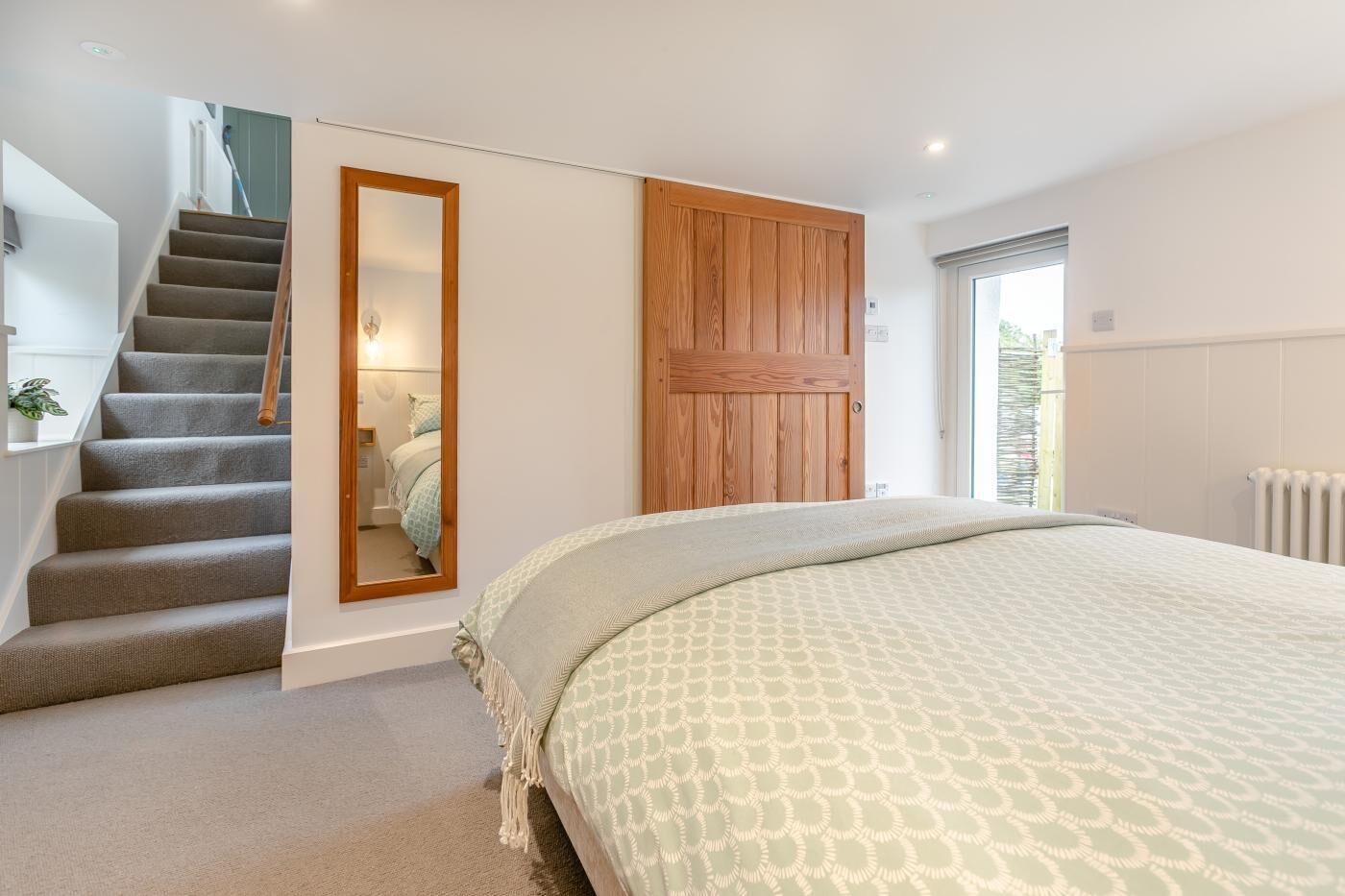 A bedroom with a bed, a wooden wardrobe, a mirror, a staircase, and a radiator.