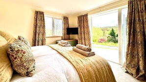 A bedroom with a large bed, a flat-screen TV, and a view of a green landscape through the window. - 2 Bed in Witheridge (oc-b29206) (Witheridge)