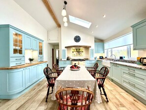 A spacious kitchen with light blue cabinets, a central island, and a dining area with wooden chairs. - 2 Bed in Witheridge (oc-b29206) (Witheridge)
