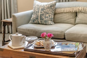 A cozy living room with a sofa, a coffee table with a tray, a teapot, a plate of cookies, and a vase with flowers.