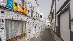 Una calle estrecha con edificios de paredes blancas con textura y puertas de madera. Se ven banderas en los edificios.